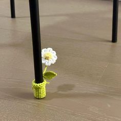 a crocheted flower in a yellow vase on the floor next to black poles