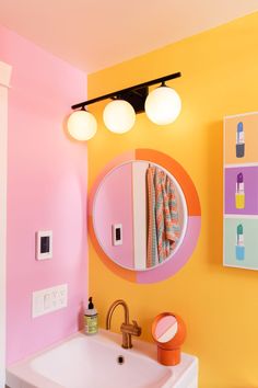 a bathroom with yellow and pink walls and a round mirror on the wall above a white sink