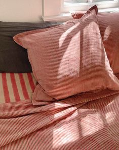 a bed with red and white striped sheets and pillows on top of it next to a window