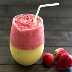 a smoothie in a glass with strawberries next to it on a wooden table