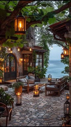 an outdoor living area with lanterns and chairs on the patio next to the water at night