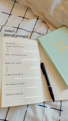 a notebook and pen sitting on top of a bed next to an open journal that says today's journal prompts