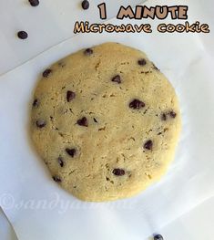 a chocolate chip cookie sitting on top of a white paper covered plate with the words 1 minute microwave cookie