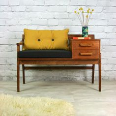 a wooden bench with a black cushion and yellow pillow on it next to a white brick wall