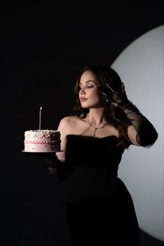 a woman in a black dress holding a pink and white cake with candles on it