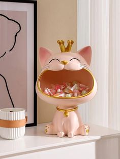 a pink cat figurine sitting on top of a white table next to a cup