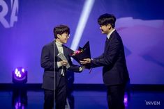 two young men standing next to each other on a stage with one holding an award