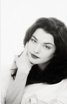 a black and white photo of a woman laying on a bed with her hand under her chin