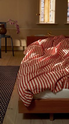 an unmade bed with red and white striped sheets on it in a living room