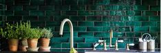 a kitchen with green tiles and potted plants on the counter top, along with copper faucets