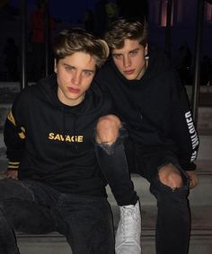 two young men sitting next to each other in front of some stairs at night time