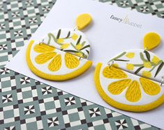 a pair of yellow and white earrings sitting on top of a piece of paper next to a card