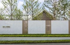 a white fence with trees and bushes around it in front of a building that has a clock on the wall