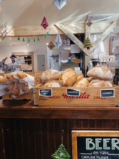 breads and pastries are on display in a bakery shop with signs hanging from the ceiling