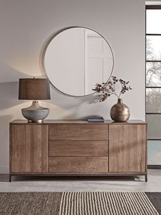 a large round mirror sitting on top of a wooden dresser next to a vase and lamp