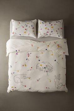 a bed with white sheets and colorful drawings on the comforter, along with two pillows