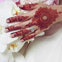 a woman's hand with henna tattoos on it and flowers in the background