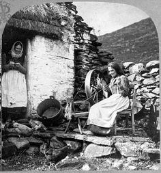 an old photo of two women sitting in front of a stone building with a wheel