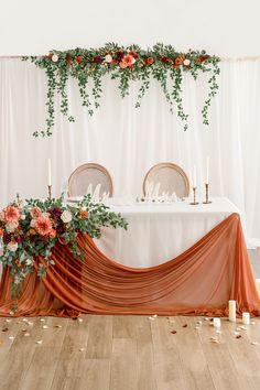 the table is set with two chairs and an orange drape draped over it, surrounded by candles