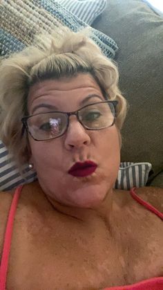 an older woman with glasses laying on a couch looking at the camera and making a funny face