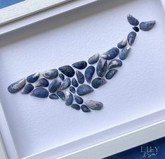 a white framed artwork with blue rocks in the shape of a bird