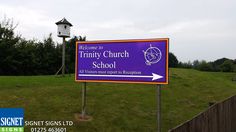 a welcome sign for trinity church school in front of a wooden fence and green grass