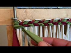 a hand is holding a piece of green and red fabric with white pins on it