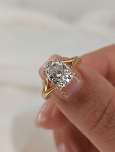 a woman's hand holding an engagement ring with a diamond in the center and a yellow gold band