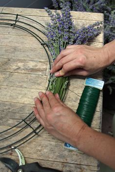 a person cutting flowers with scissors on a wooden table next to lavenders and wire