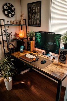 a desk with a computer, speakers and plants on it in front of a window