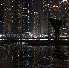 a person standing in front of a city at night with buildings reflected in the water