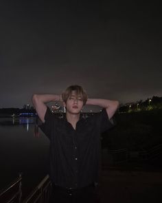 a young man standing next to a body of water with his hands on his head