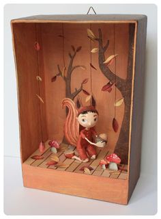 a wooden box that has a doll in it and some leaves on the tree branches