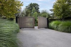 an open gate in the middle of a driveway surrounded by tall green grass and trees