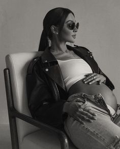 a black and white photo of a pregnant woman sitting in a chair with her hands on her stomach