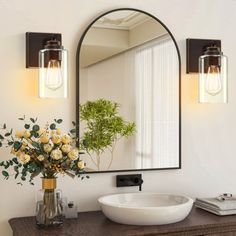 a bathroom with a sink, mirror and flower vase on the counter in front of it