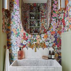 a bathroom sink sitting under a mirror in front of a floral wallpapered wall