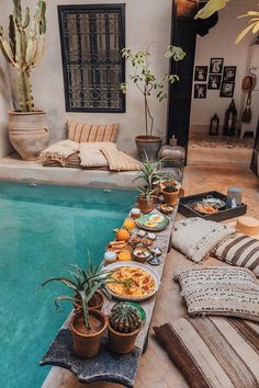 an indoor swimming pool with plants and food on the table next to it, surrounded by potted cacti