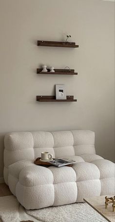 a living room with a white couch and two shelves on the wall, coffee table in front of it