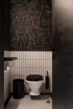 a black and white toilet in a bathroom next to a wall with designs on it