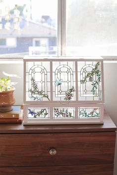 a wooden dresser topped with a vase filled with flowers next to a stained glass window