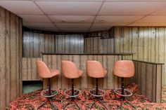 four pink chairs sitting on top of a carpeted floor next to a wooden wall