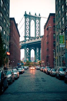 cars are parked on the street in front of tall buildings with a bridge above them