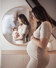 a pregnant woman standing in front of a mirror with her baby girl looking at herself