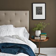 a bed with white sheets and pillows next to a small table with books on it