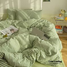 a laptop computer sitting on top of a bed covered in green and white striped sheets