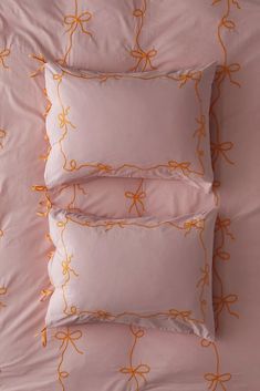 four pillows with orange bows on them are lined up against a pink bed sheet and pillowcase