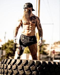 a shirtless man standing on top of a tire with his hands in his pockets