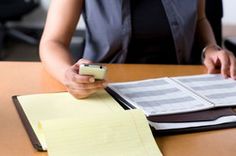 a person sitting at a desk with a cell phone in their hand and papers on the table