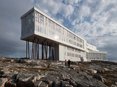 a white building sitting on top of a rocky beach next to the ocean with people walking around